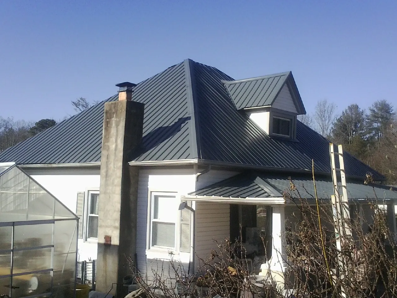 Dark blue standing seam metal roof on a white farmhouse with dormer — Slate & Tile Roof Repair by Roofing Brothers in Monarch