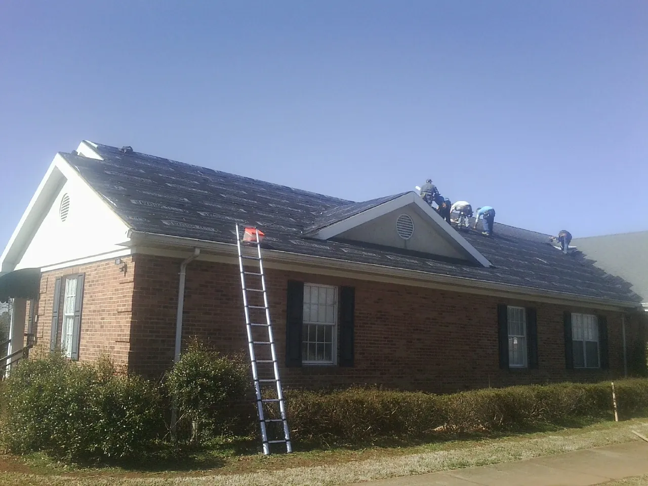 Crew tearing shingles off a brick ranch roof with a ladder set — Emergency Roof Repair work by our crew in Monarch