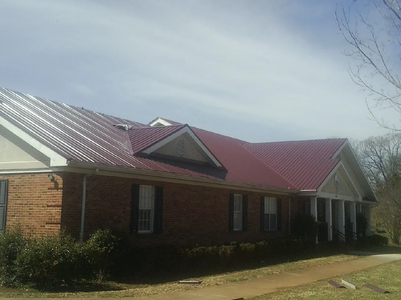 Red metal roof with gabled entries on a long brick building, from a Hail Damage Roof Repair job in Monarch