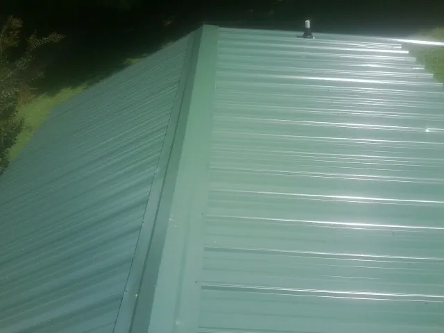 New green metal panels meeting at the ridge of a roof — Flat Roof Repair work by our crew in Monarch