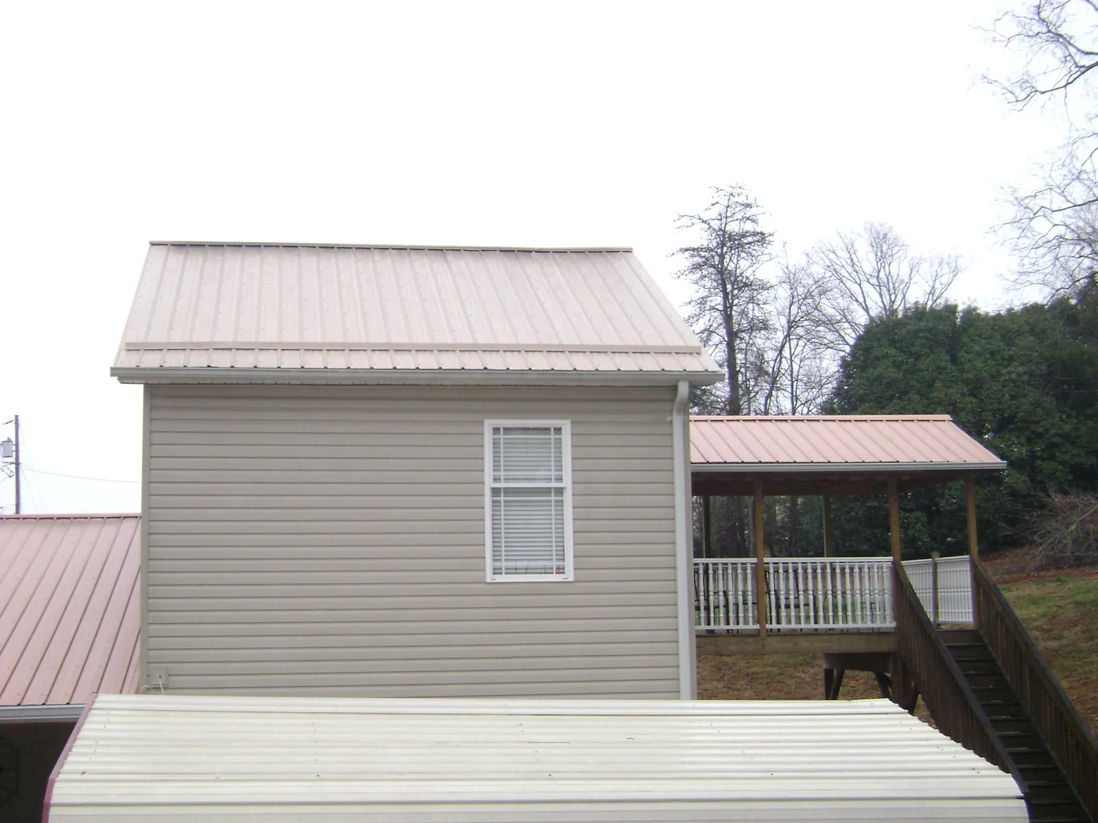 Tan metal roofs on a two story addition and attached porch, from a Roof Replacement job in Monarch